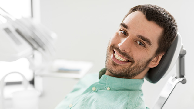 A man sitting in a dental chair, smiling and looking directly at the camera.